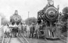 Group of men and boy on tracks in front of steam engine